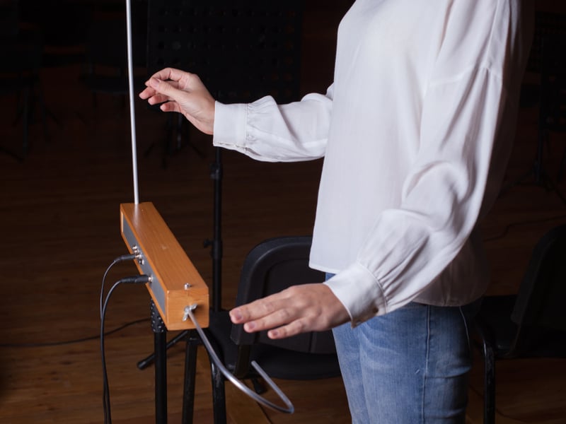 An electronic music instrument, the Theremin, is on a stand on a stage with a performer stood with their hands ready to play it.