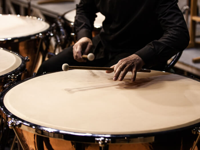 Timpani player sits at a drum, hands visible only