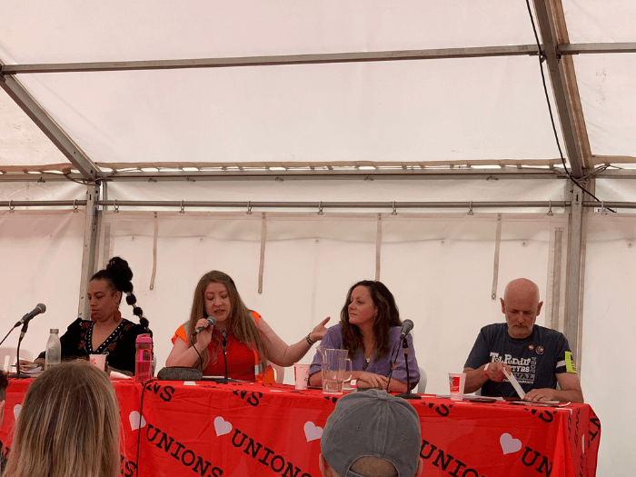 A panel event from last year in a tent. There are four people sat along a table in front of a crowd.