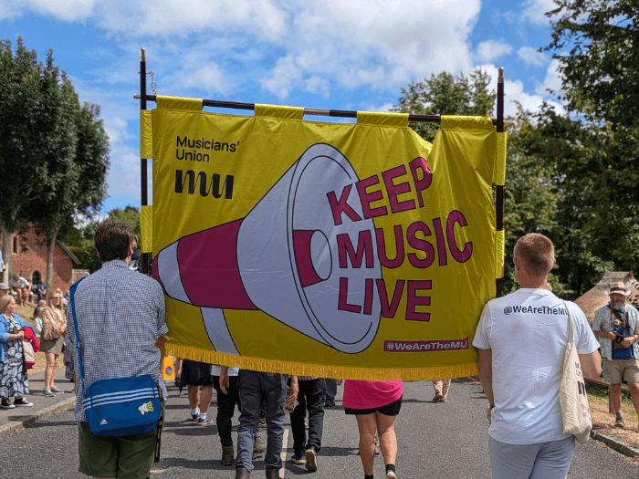 The new MU banner - a large yellow silk design with logo and pink megaphone saying 'keep music live' - being carried by two people in the procession.