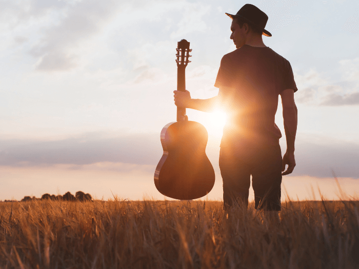 Silhouette of musician with acoustic guitar at sunset in a field.