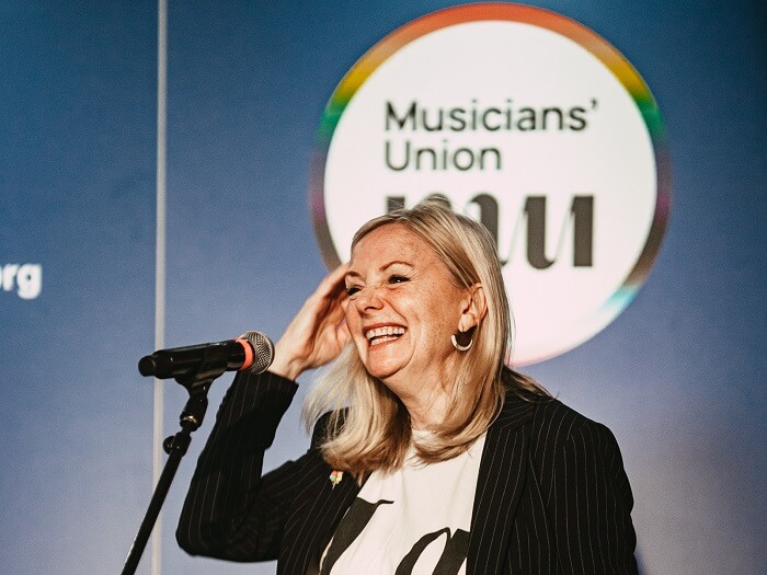 Mayor Tracy Brabin speaking at the MU Members' Conference, she's smiling broadly and the MU Equalities logo is behind her.