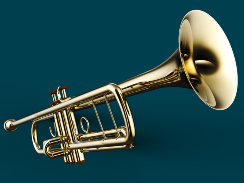 Photograph of a trumpet in front of a dark green background.