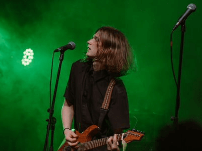 A guitarist performing on stage and singing into a microphone.