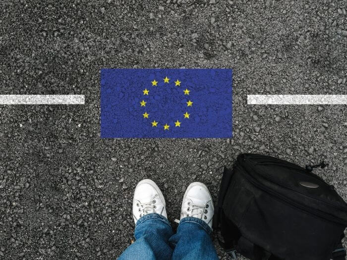 Birdseye view of feet staring down at an EU flag on the ground, representing a border.