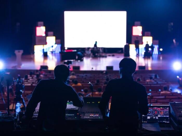 Silhouette of two sound engineers, in front of empty stage at a mixing desk.