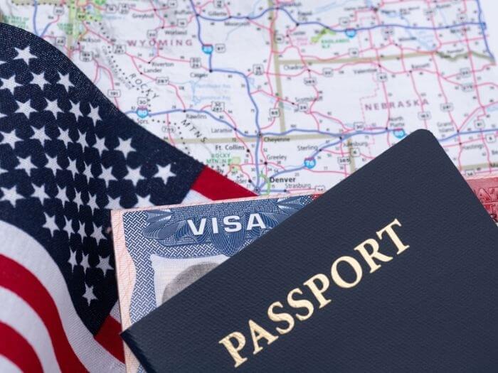 A passport and visa and US flag on top of a map of the United States.