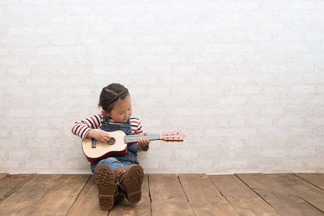 Photograph of a small child sat learning the Ukulele