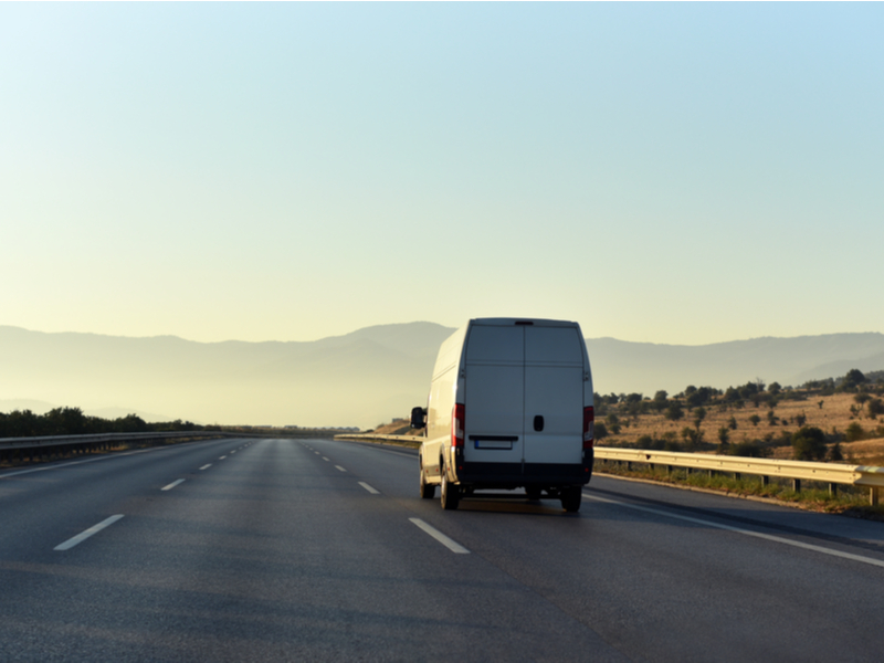 Photograph of a transit van driving down an empty road, beautiful mountain scenery is in the misty background.