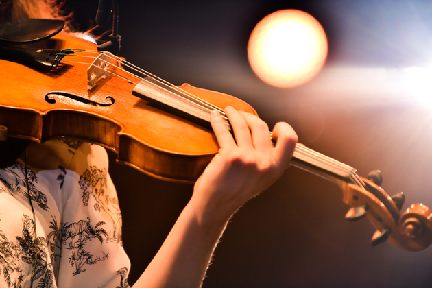 Photograph of a violinist playing, the background is blurred and the person is not visible apart from their arm and shoulder