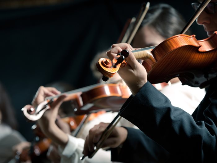 Symphony orchestra violinists performing on stage against dark background.