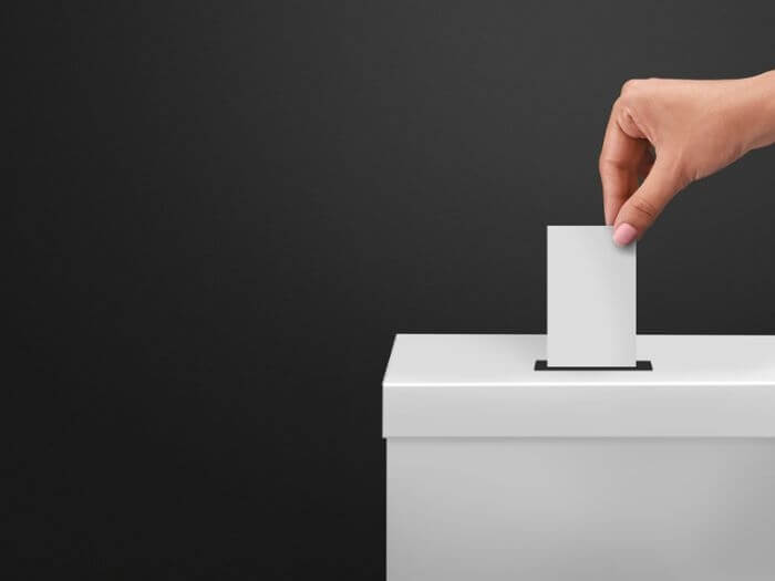 Hand putting a blank white slip into a white sealed box, representing voting.