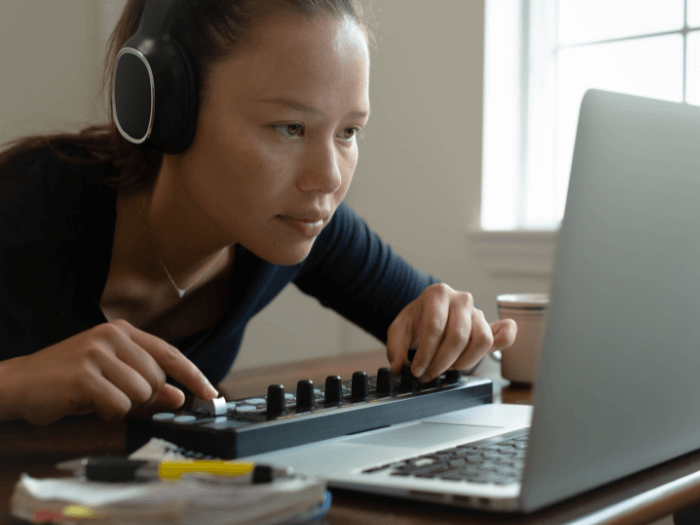 A woman wearing headphones and making music using her computer at home.