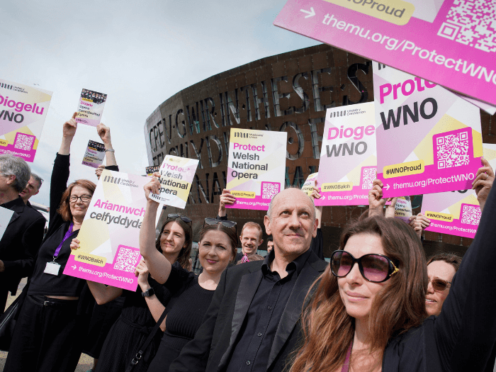 People holding 'protect WNO' posters outside of The Wales Millennium Centre.