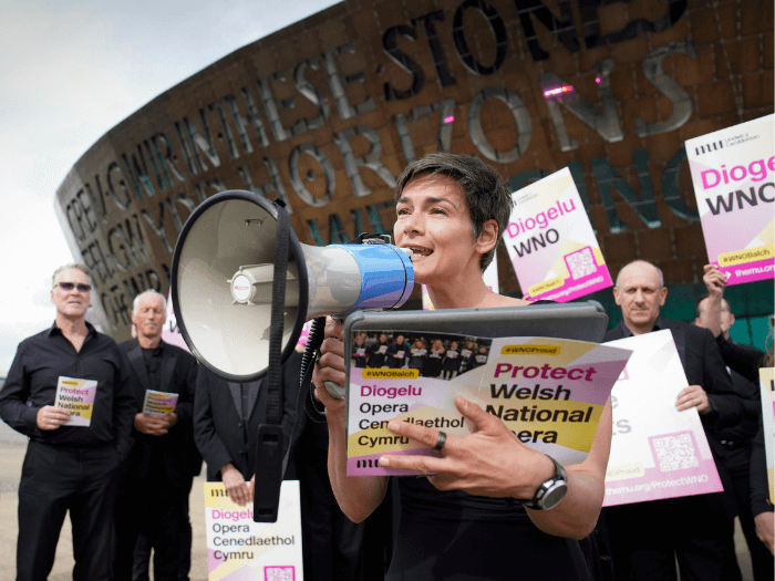 Members of the WNO orchestra stood outside the Wales Millennium Centre at a leafleting demo event in June. One person is holding a megaphone.