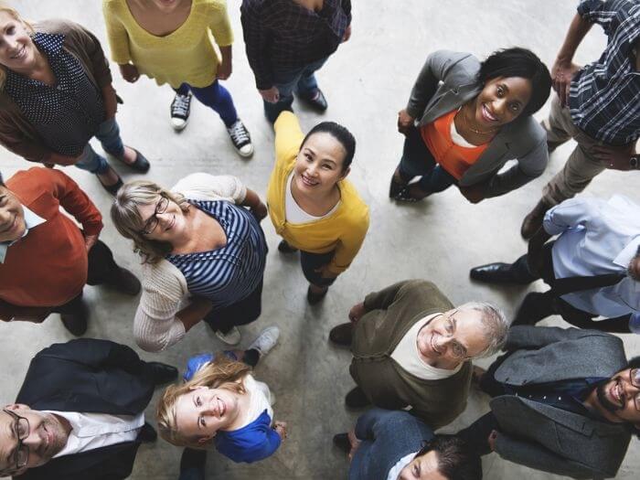 Group of people, men and women, young and old, grouped together and smiling, looking up at the camera above.
