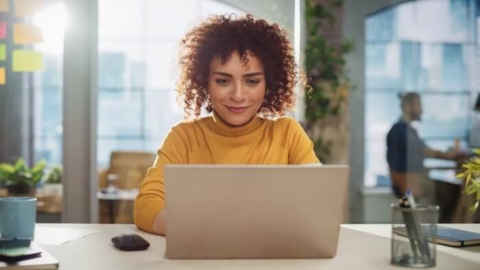 Woman sat at a desk in front of an open laptop smiling.