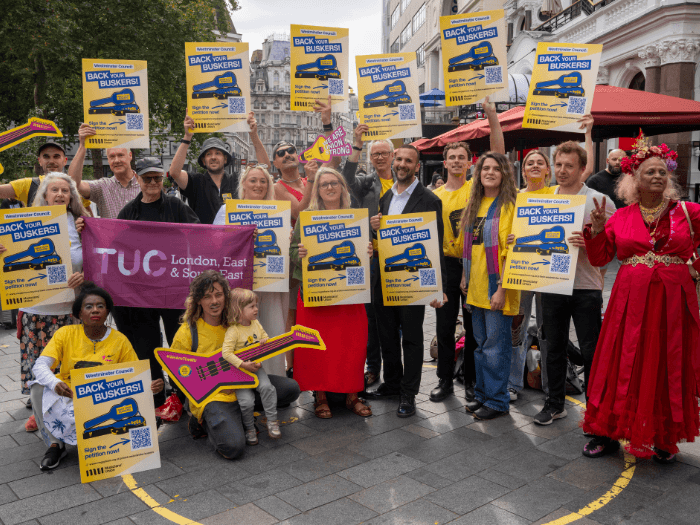 Naomi Pohl, Zack Polanski, MU members and staff, and buskers gathered in a group holding yellow placards saying ‘Westminster Council, back your buskers!’.