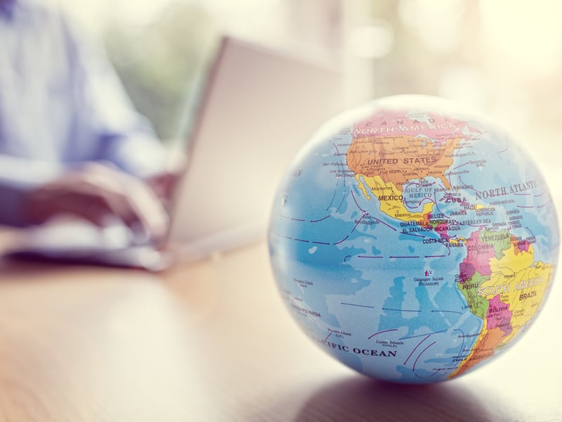 Photograph of a small globe on a desk, with a man working at a laptop in the background out of focus