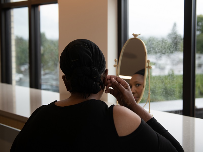 A woman is looking in the mirror and adjusting her hearing aid in the mirror.