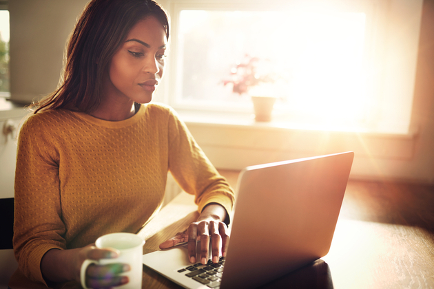 Photograph of a woman sat looking intently at a laptop, golden light on a home office setting in the background