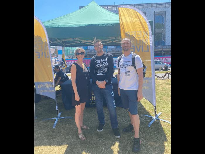 The three MU Midlands staff at last year's festival, stood in front of the Union's stand and yellow flags on a bright sunny day.