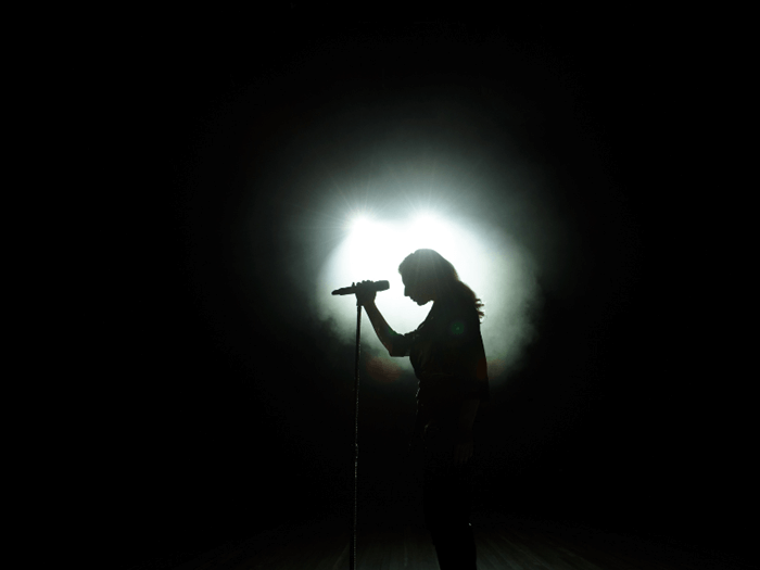 Blacked out image with a single spot light in center where a women's silhouette is singing into a microphone.