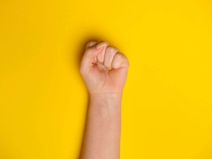 Woman’s fist against a bright yellow background. Women's equality and rights concept.