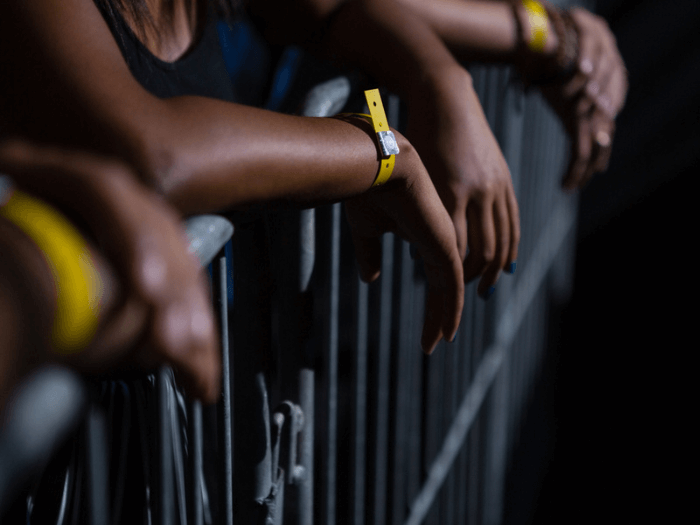 Close up of crowd with hands draped over a metal stage barrier, wearing yellow festival wristbands.