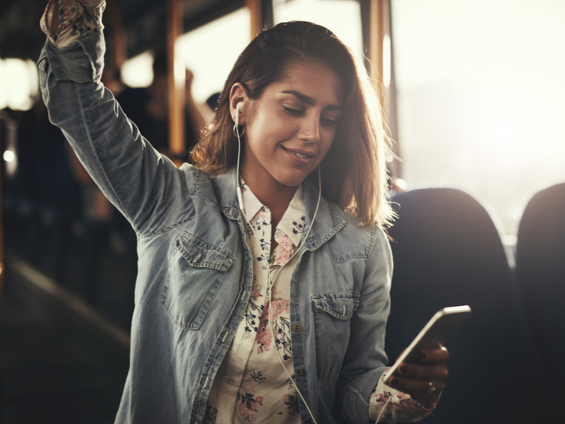 Photograph of a young woman listening to music off her phone on the bus.