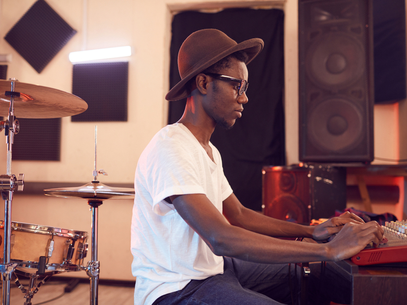 Young musician working in a studio, he is sitting at a mixing desk, behind him a drum kit is visible