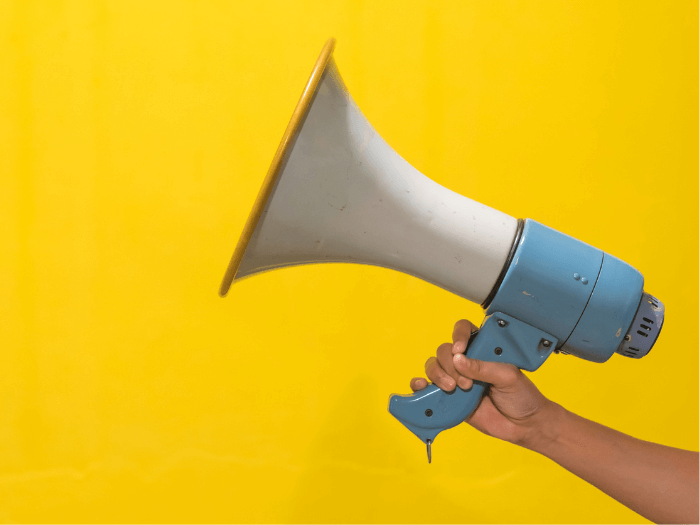 Woman's hand holds megaphone with yellow background.