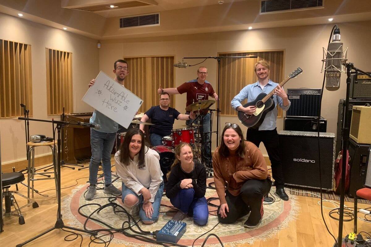 Members of the Youth Music Future Collaborations team in a recording studio space, smiling and holding instruments with some of the participants.