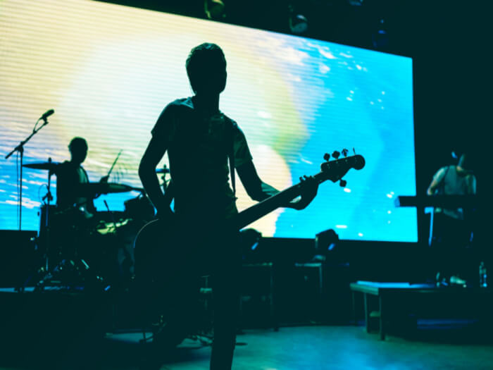 A band plays on a stage silhouetted against the a bright blue background.