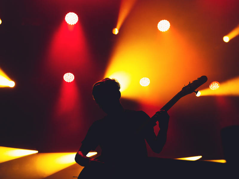 Electric bass guitarist performs on stage, we can only see their silhoutte outlined against orange and red lights