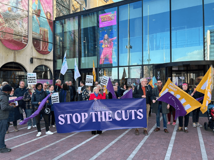 A protest in Birmingham against city council cuts, with protesters waving flags and holding banners.