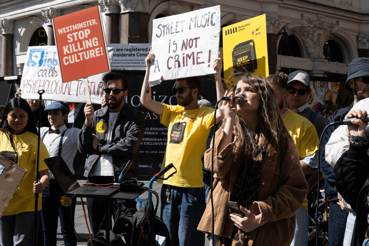 A photo of musicians at a protest in Leicester Square, holding up banner and signs.