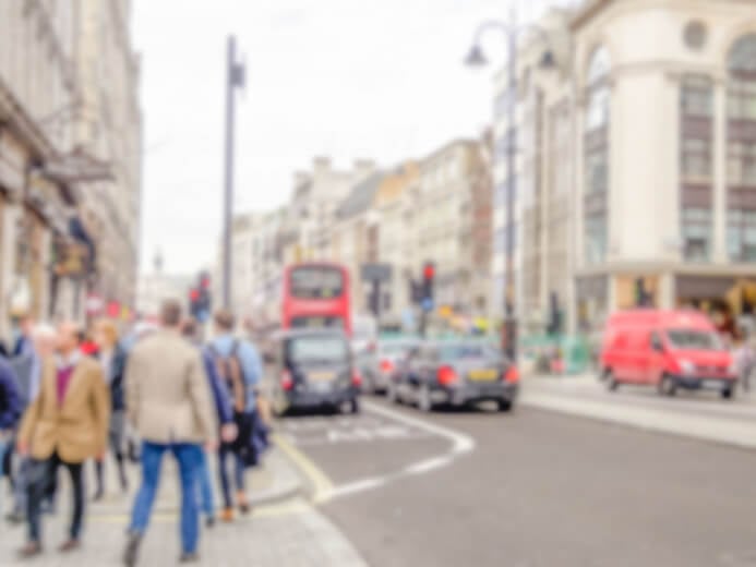 Out of focus picture of a busy UK high street with cars, taxis and pedestrians visible.