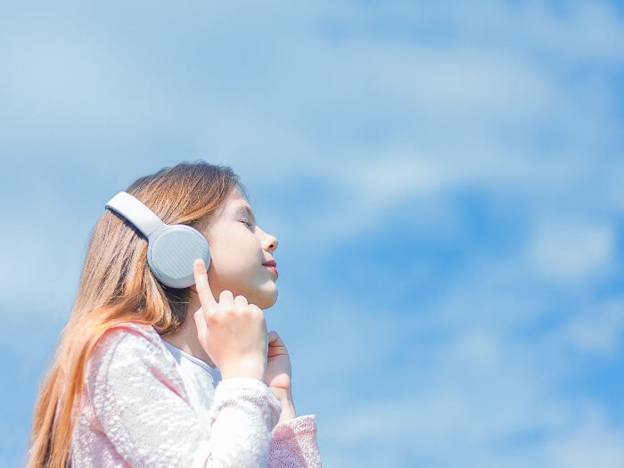 A child enjoys listening to music through a pair of large grey headphones against a slightly cloudy blue sky