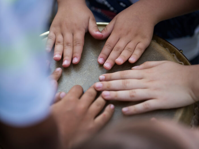 The hands of small children playing on a singular djembe drum