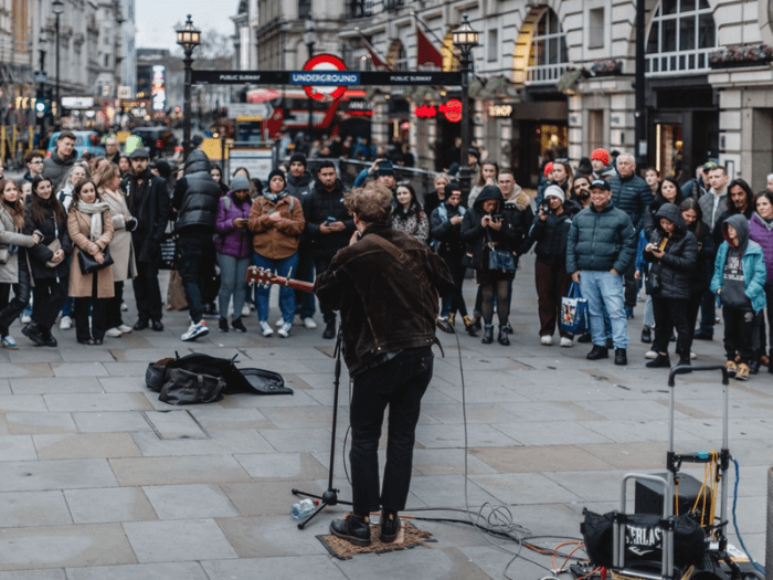 A musician busking on the street with a crowd around him.