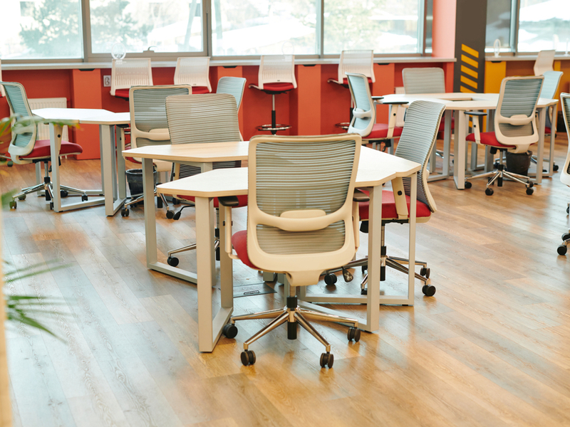 An empty training room, or open plan office. A number of chairs are pulled up to empty desks set out in circular shapes.