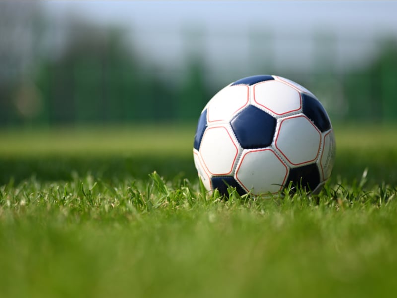 Photograph of a football in a grassy field, the sun is shining and the grass is green.