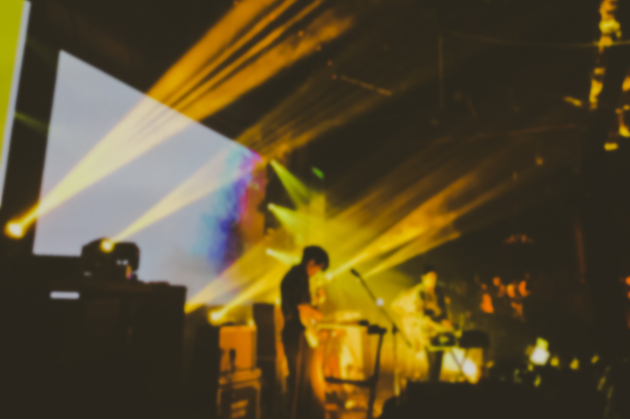 Photo of a concert happening indoors at a grassroots music venue, with the band silhouetted against yellow stage lights.