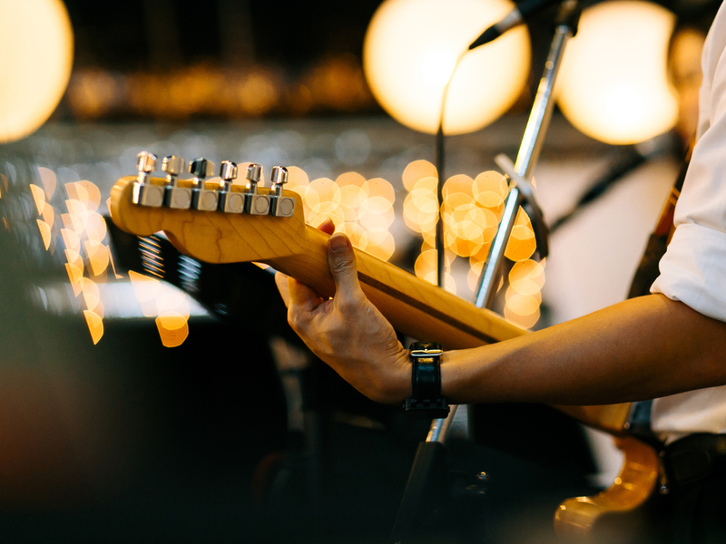 A guitar player in a function band, we can see the back of the neck of an electric guitar looking out over a blurred audience