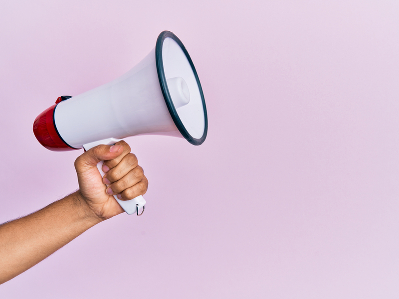 A outstretched hand holding a megaphone against a lilac background.