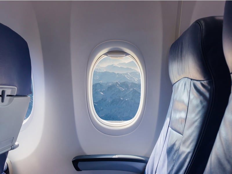 Photograph taken through a set of empty plane seats, through the window a snow capped mountain range is visable.
