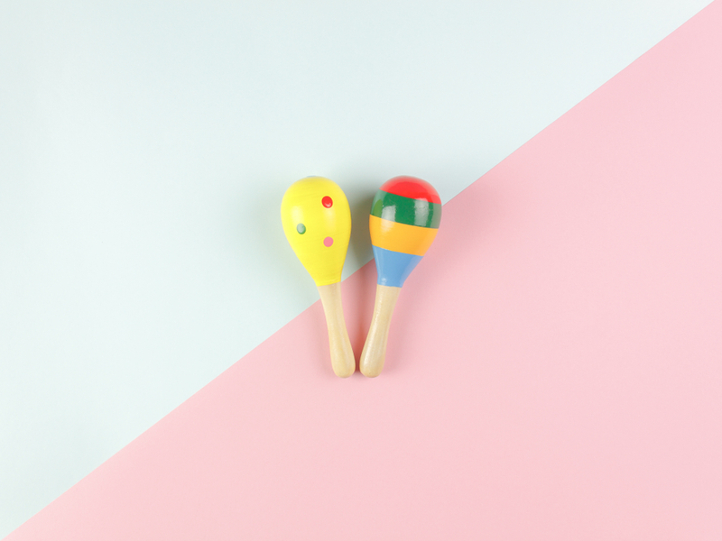 Photograph of a pair of brightly painted miniature maracas against a blue and pink background.