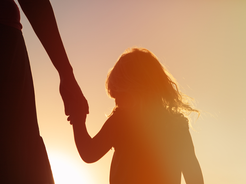 Silhouette of a mother and daughter stood against a bright light.