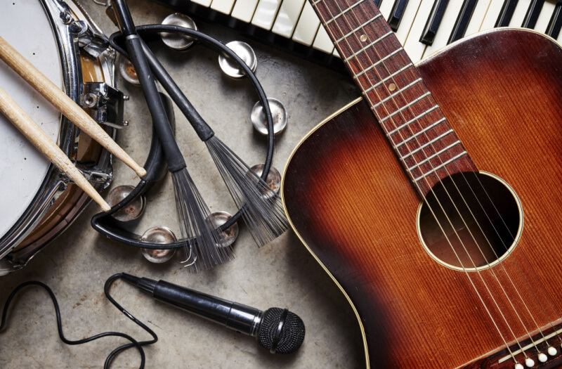Multiple instruments including a microphone, an acoustic guitar and a drum, laid out on a grey surface.